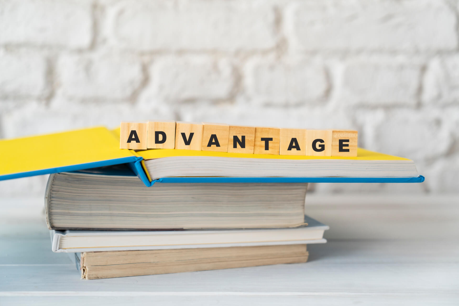 wooden blocks spelling advantage on top of a stack of books